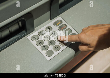 Woman finger pressing key on a street cash machine keyboard in a sunny day at Merida. The city preserves many buildings of ancient Rome in Spain. Stock Photo