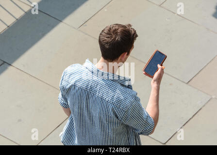 A young man holding his smartphone whilst texting, London, UK Stock Photo