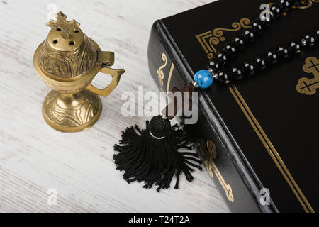 Closeup of Holy Bible, rosary beads with cross and incense burner on white wooden background. Religion concept and faith. Stock Photo