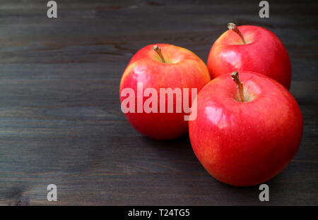 Three red apples on dark colored wooden table with free space for text and design Stock Photo