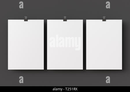 Three blank paper posters hanging on binder clips on black wall background Stock Photo