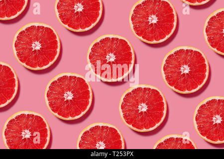 Colorful fruit pattern of fresh grapefruit slices on pink background. Minimal flat lay concept.