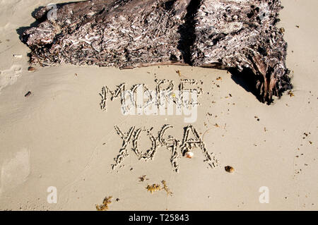 Text "More Yoga" written in the sand, with a tree trunk above made on Otres Beach, Cambodia Stock Photo