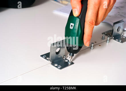 Woman hand with screw drill twisting the screw into the furniture. Close-up. Stock Photo