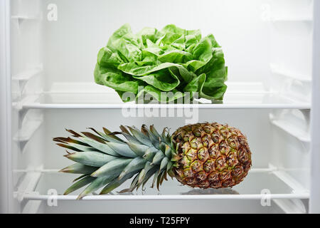 Lettuce and pineapple on shelf in refrigerator. Fridge with open door, close up. Stock Photo