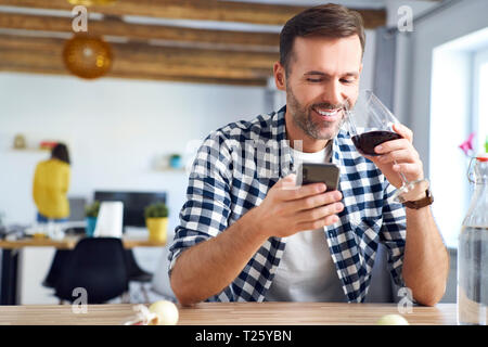 Man sitting at table, using smartphone, relaxing with a glass of red wine Stock Photo