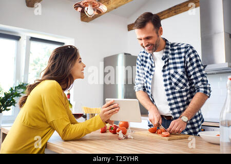 Affectionate couple in kitchen, preparing spaghetti toghether, using digital tablet Stock Photo