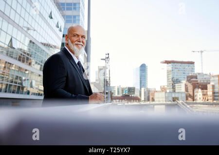Elegant businessman leaning on railing  in the city, smiling Stock Photo