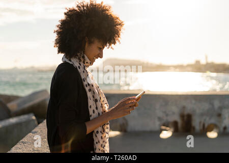 Smiling woman using smartphone near the sea Stock Photo