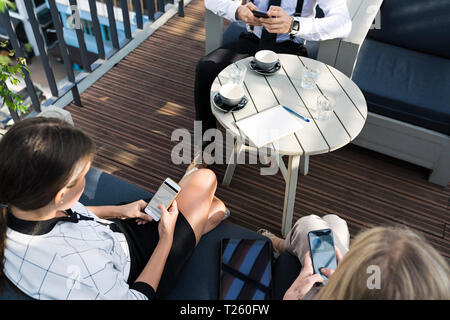 Three business colleagues having a coffee break on city terrace checking smartphones Stock Photo