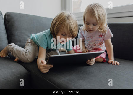 Brother and little sister using digital tablet on the couch at home Stock Photo