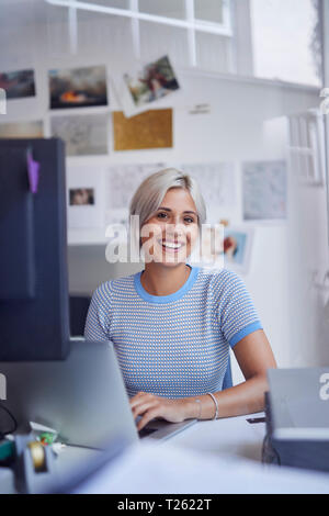 Young woman working in office, sitting at desk, smiling Stock Photo