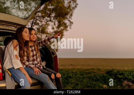 Two sisters sitting at opened tail watching sunset together Stock Photo