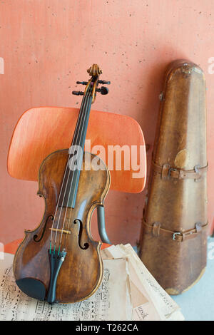 Violin and sheet music on wooden chair with violin case in the background Stock Photo