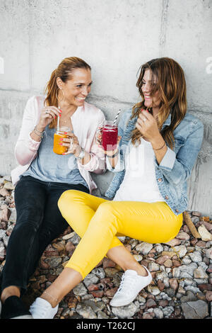 Two female friends drinking smoothies outdoors having fun Stock Photo