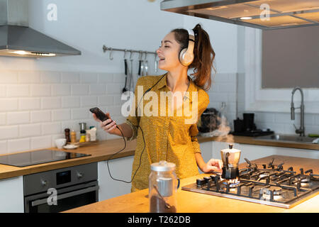 Young woman listening musuc in the kitchen, while preparing her morning coffee Stock Photo
