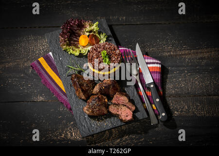 Kangaroo steak with red rice and mango on slate plate Stock Photo
