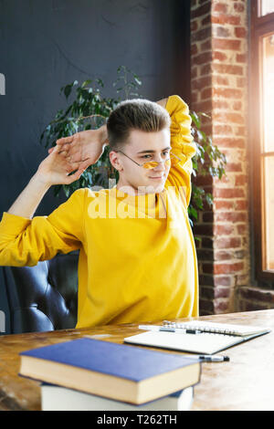 Blonde student in glasses wearing yellow pullover relaxing while preparing for test or exam Stock Photo