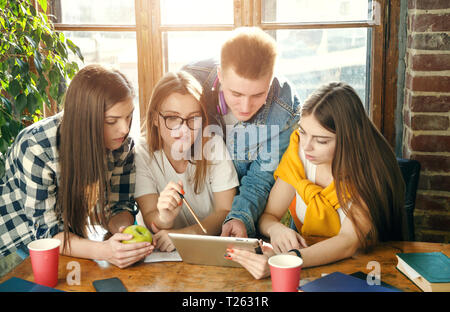 Group of classmates sitting at the desk, looking at the tablet and discussing something Stock Photo