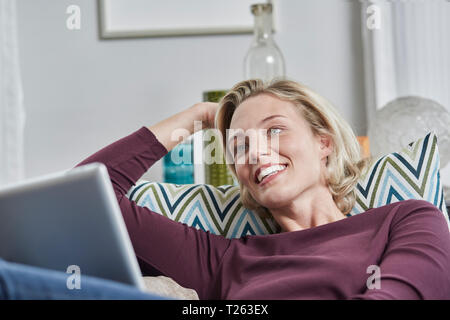 Smiling young woman with tablet lying on couch at home Stock Photo