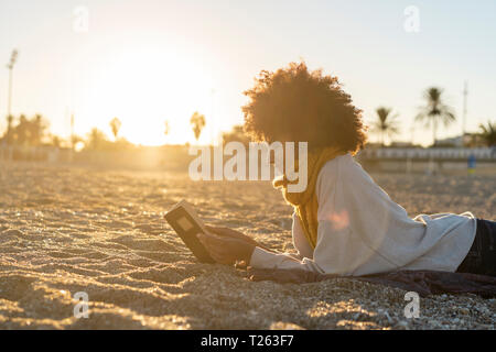 Woman lying in the sand, relaxing on the  beach, reading a book Stock Photo