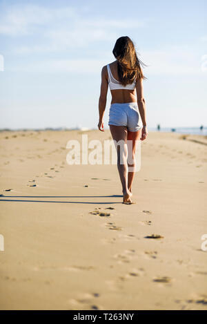 Rear view of woman walking in sand on the beach Stock Photo