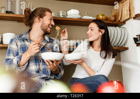 Happy couple sitting in kitchen, eating spaghetti Stock Photo