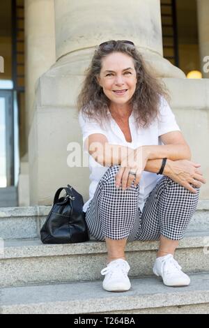 Portrait of smiling mature woman sitting on stairs in summer Stock Photo
