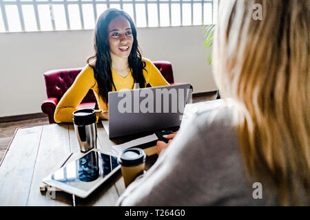 Two young businesswomen talking at conference table in office Stock Photo