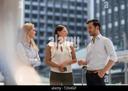 Smiling business colleagues talking in the city in front of skyscraper Stock Photo