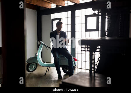 Man with motor scooter in a loft using cell phone Stock Photo