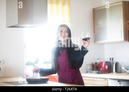 Young woman cooking at home holding glass of red wine Stock Photo