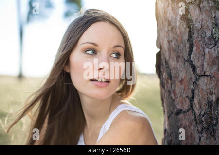 Portrait of young woman leaning against tree trunk Stock Photo