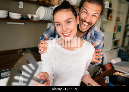 Young couple preparing food together, laughing and pointing with spatula Stock Photo