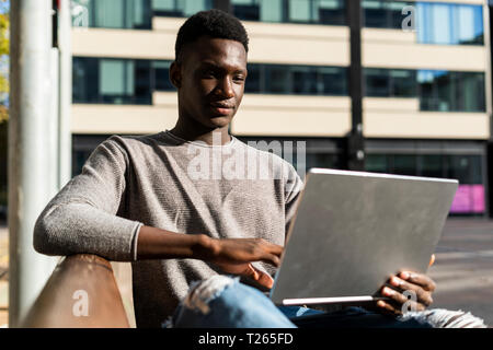 Young man sitting on a bench in the city, using laptop Stock Photo