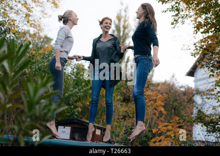 Happy mother with two teenage girls jumping on trampoline in garden in autumn Stock Photo