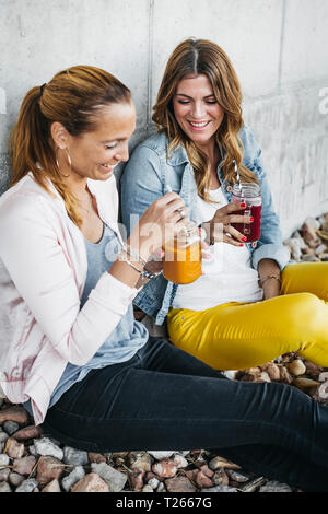 Two female friends drinking smoothies outdoors having fun Stock Photo
