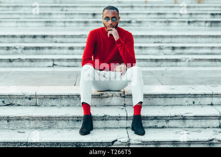 Portrait of stylish young man wearing red pullover and socks sitting on stairs Stock Photo