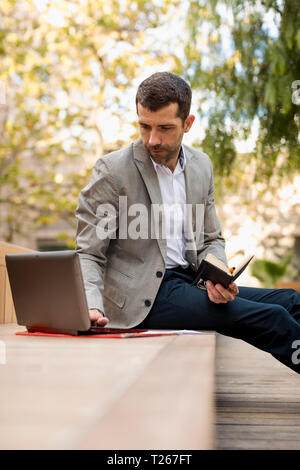 Businessman sitting on a bench using laptop and diary Stock Photo