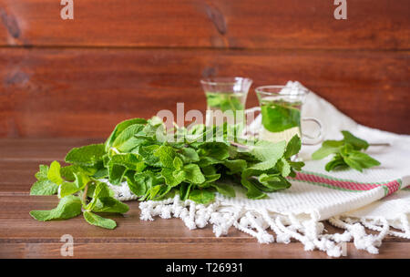 Mentha leafs with small glass tea cups on behind  on wooden background Stock Photo
