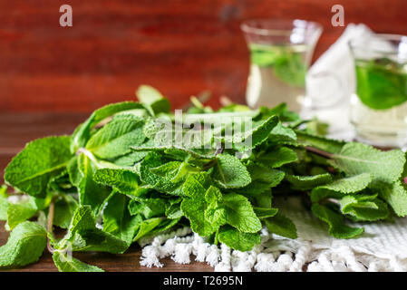 Mentha leafs with small glass tea cups on behind  on wooden background Stock Photo