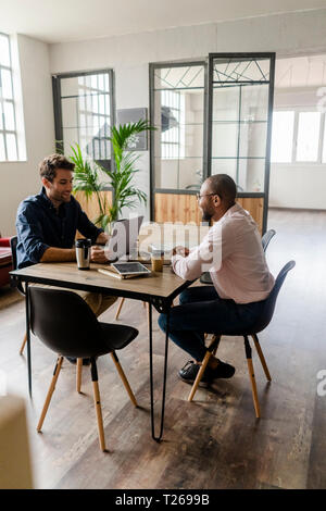 Two young businessmen talking at conference table in loft office Stock Photo
