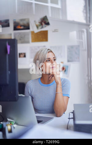 Young woman working in office, sitting at desk, smiling Stock Photo