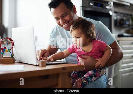 Smiling father and baby girl using laptop on table at home Stock Photo