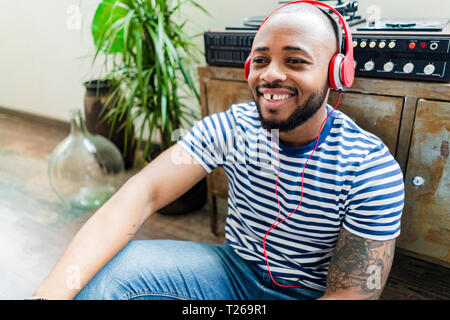 Happy young man with headphones sitting on floor in a loft Stock Photo