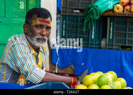 A bearded man with a tilaka in a street market selling lemons and fruit Stock Photo