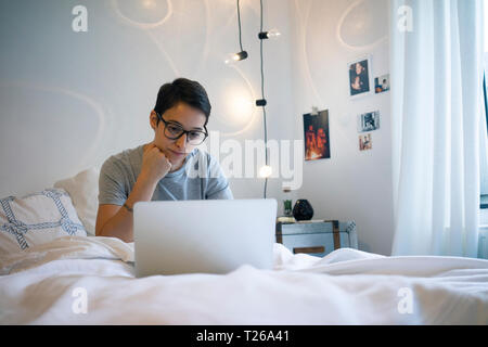 Young woman sitting in bed, using laptop Stock Photo