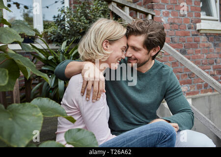 Happy couple sitting on stairs cuddling Stock Photo