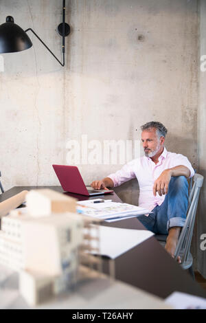 Businessman in a loft using laptop with documents and architectural model on table Stock Photo