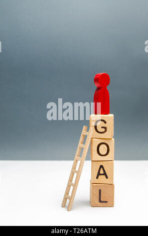 The red figure of a man stands on a tower of cubes with the word goal. The concept of achieving the goal, dedication and diligence, overcoming obstacl Stock Photo